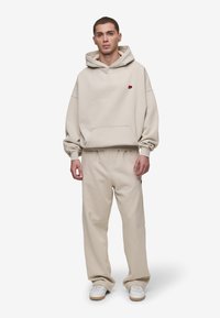 Sweatshirt bege com capuz e bolso frontal, acompanhado por calças de moletom bege combinando. Tecido suave com corte descontraído.