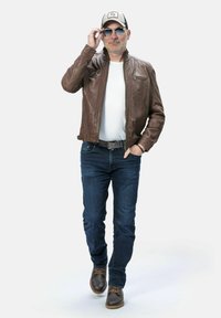 Bruine leren jasje, wit T-shirt, blauwe jeans en bruine laarzen. Accessoires omvatten een zonnebril en een lichtgekleurde pet.