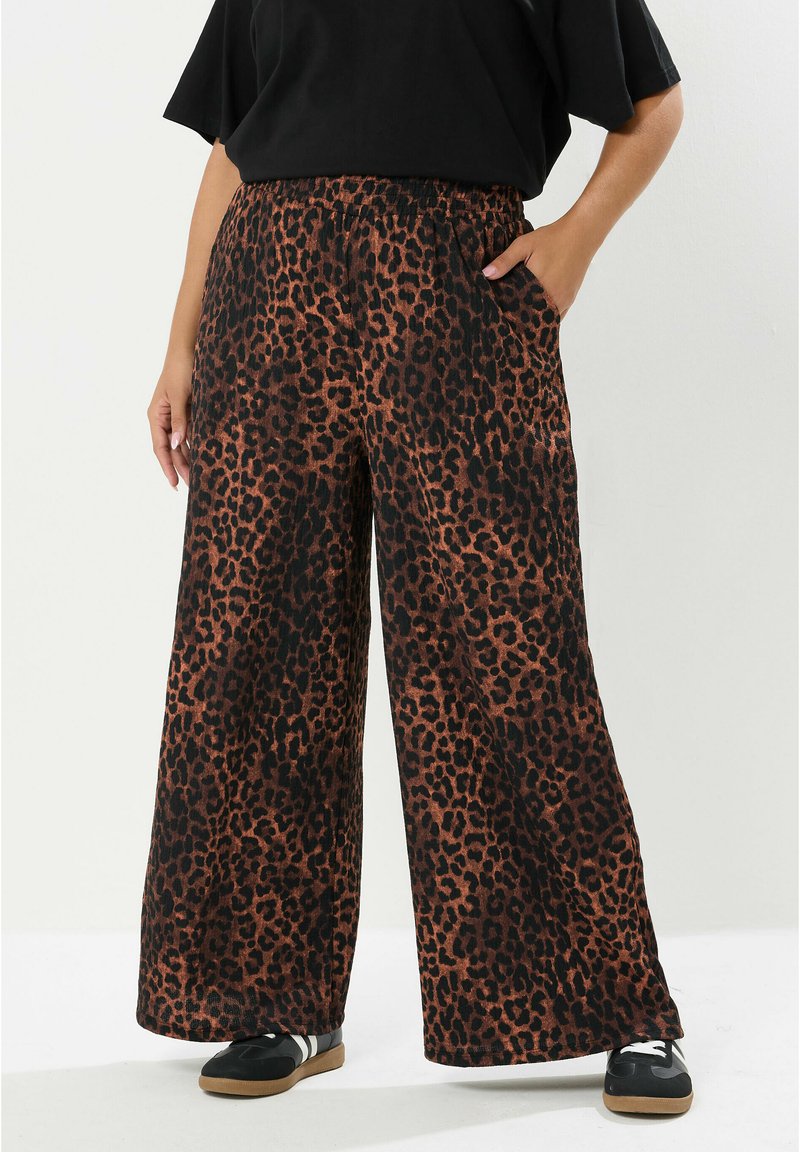 Leopardenmuster weite Hose aus braunem und schwarzem Stoff, mit elastischem Bund und seitlichen Taschen. Kombiniert mit schwarzen Sneakers.
