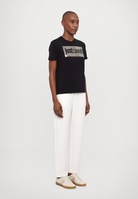 Svart bomull t-skjorte med et metallisk dyreprint-panel og "just cavalli" tekst. Kombinert med hvite bukser og nøytrale sneakers.