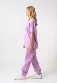 Lilac pārmērīga T-kreklā un atbilstošajās joggerbiksēs, abi izgatavoti no mīkstas kokvilnas. Raksturīga brīva piegriezuma un elastīgas aproces. Saderībā ar masīviem baltiem sporta apaviem.