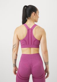 Sostén deportivo rosa con diseño de espalda de nadador, fabricado en tejido texturizado, combinado con leggings de tiro alto a juego que presentan acentos de costura curva.