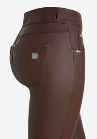 Pantalones de cuero sintético marrones con cintura alta, ajuste ceñido, bolsillos traseros con acentos de metal plateado y detalles cosidos a lo largo de las costuras.