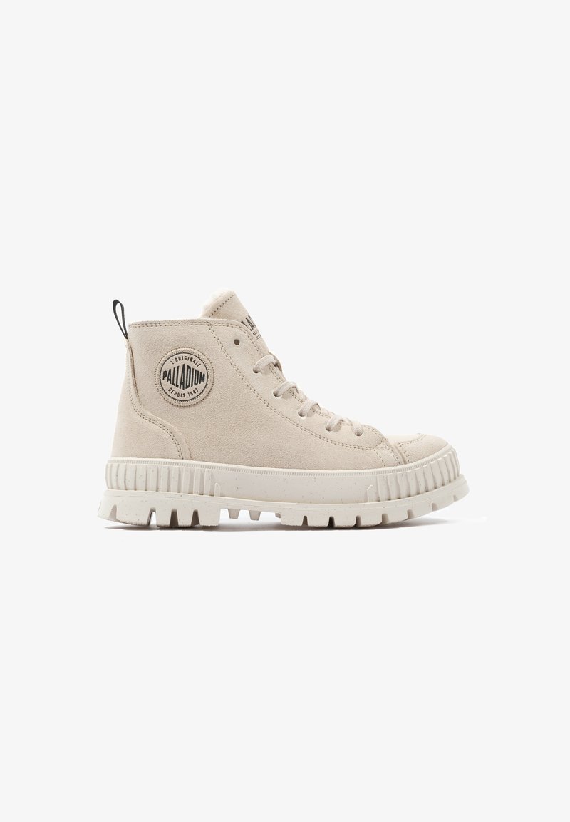 Bottines en suède beige, à bout rond, avec une semelle en caoutchouc texturé et un patch logo circulaire sur le côté extérieur. Une tirette à l'arrière est incluse.