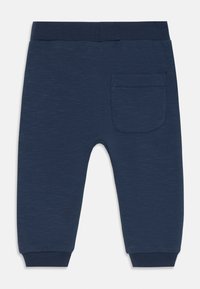 Marineblå joggebukser laget av mykt, strukturert stoff. Har en tettsittende midjebånd og en enkelt baklomme med sømdetaljer.