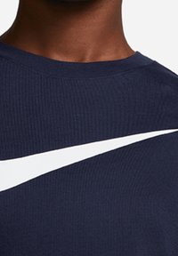 Marinblå ribbad T-shirt i bomullsblandning med en stor vit Nike Swoosh-logotyp över bröstet. Rund halsringning, kortärmad.