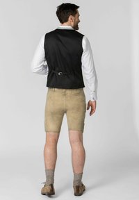 Black satin waistcoat with back adjuster, paired with beige shorts. White long-sleeve shirt visible underneath. Woolen socks and shoes complete the look.