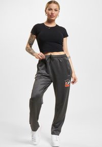 Grå svedpants med snøre i taljen, med et grafisk logo i orange og sort. Sammen med en tætsiddende sort crop top og hvide sneakers.