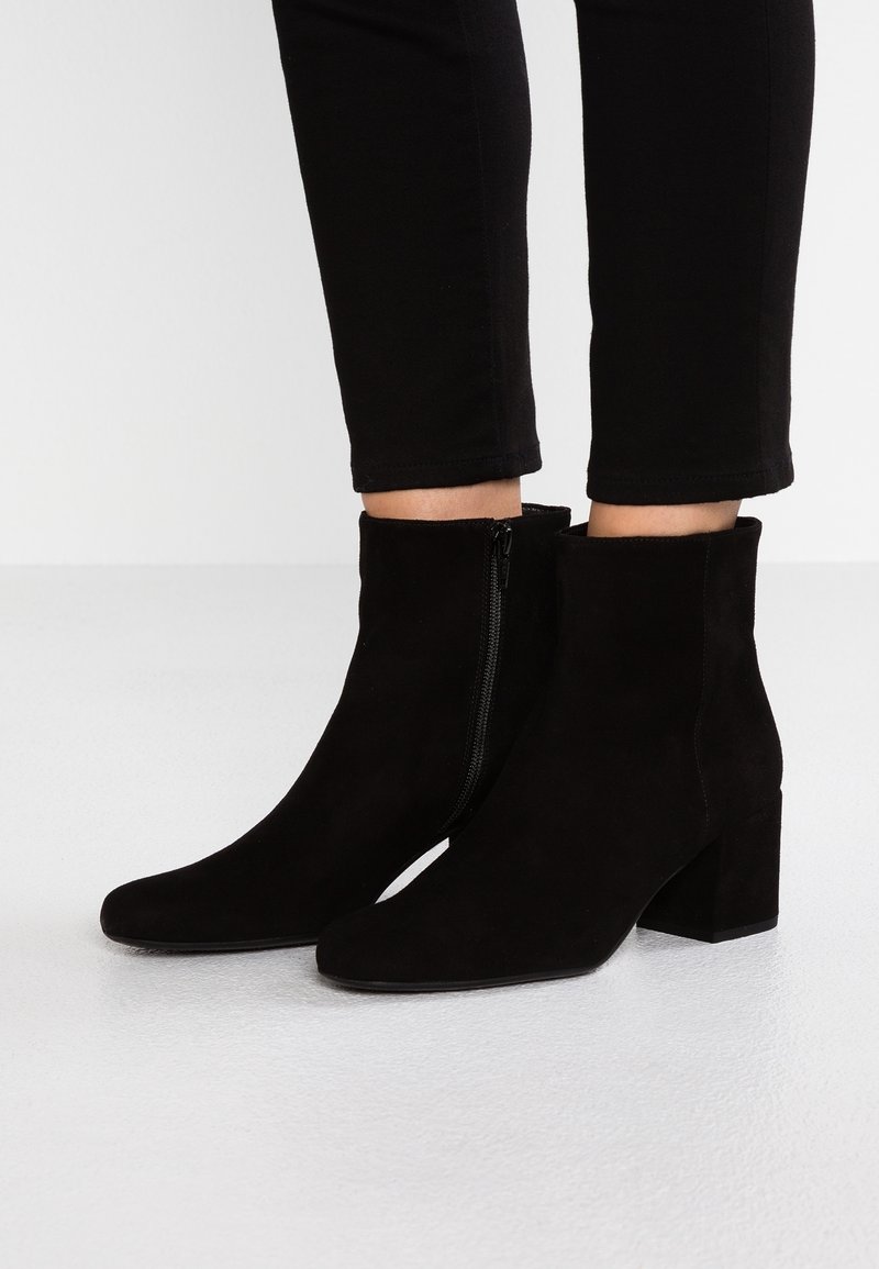 Bottes courtes en daim noir avec talons carrés et fermetures éclair latérales portées avec un pantalon noir ajusté.