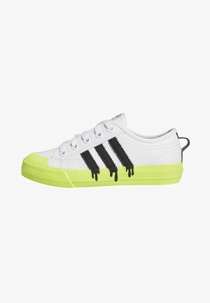 Biały niskoprofilowy sneaker z neonowo-żółtą podeszwą i czubkiem, z trzema czarnymi ociekającymi paskami po boku oraz białymi sznurowadłami.
