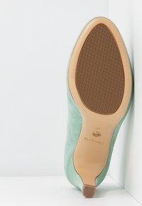 Chaussure en daim vert avec une finition lisse, un bout pointu et une semelle en caoutchouc marron à motif. Présente un petit talon accentué et un marquage de taille.