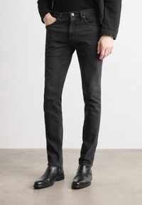 Black slim-fit jeans made of denim feature a mid-rise waist, five-pocket design, and subtle stitching. Paired with black ankle boots.