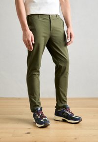 Olivenfarvede bukser i bomuld med slim fit og en glat tekstur. Bæret med marineblå sneakers med lilla accenter og hvid detaljer.