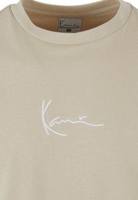 Tricou de bumbac bej cu guler rotund și mâneci scurte. Prezent e un logo alb brodat subtil pe față.