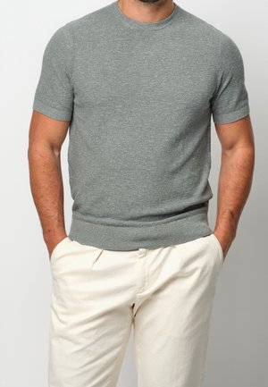 Pull gris à manches courtes en maille avec un col rond, un ourlet côtelé et une texture lisse, assorti à un pantalon de couleur claire.