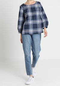 Blusa a quadri navy con scollatura quadrata e maniche lunghe a sbuffo, abbinata a jeans azzurri a vestibilità ampia e sneakers bianche.
