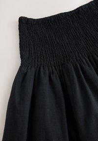 Robe noire avec un corsage froncé et une jupe évasée. Le tissu a une texture douce et une finition lisse, avec un design fluide.