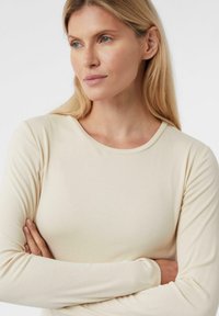Beżowa bluzka z długim rękawem, wykonana z miękkiego, gładkiego materiału, z okrągłym dekoltem i dopasowanym krojem, o prążkowanej fakturze.