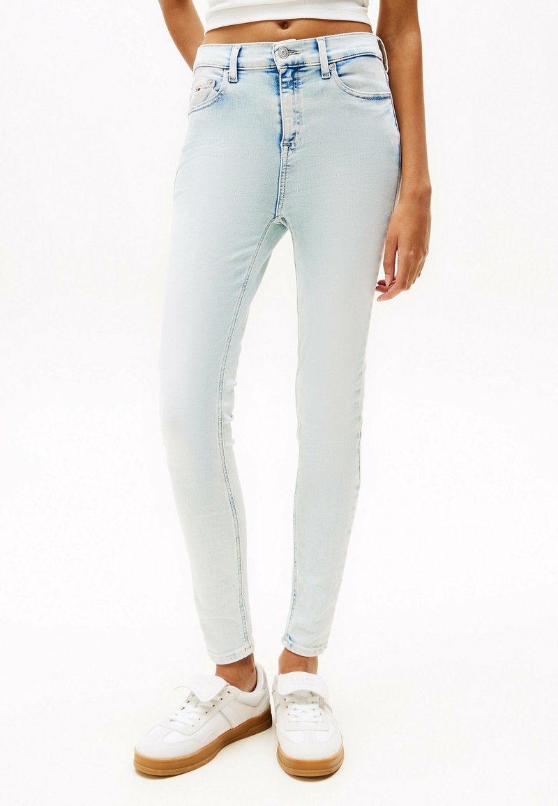 Jeans ajustados de color azul claro, confeccionados en denim, con cierre de botón, bolsillos frontales y un acabado desgastado con costuras visibles.