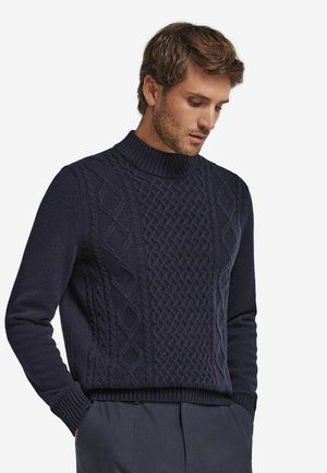 Maglione lavorato a maglia blu navy con un alto colletto, modelli a trecce testurizzati e polsini a coste. Il design è uniforme e presenta una forma squadrata.
