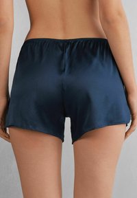 Marina satingshorts med elastiskt midjeband, med en slät textur och kort fåll. Bakvy som visar en enkel design och snitt.