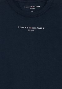 Mørkeblå bomulls T-skjorte med rund hals, korte ermer og hvit logo med teksten: "TOMMY HILFIGER EST. 1985" nær halslinjen.
