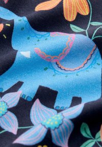 Katoenen stof met een blauwe olifant met kleurrijke bloemmotieven, geplaatst tegen een zwarte achtergrond met levendige oranje en roze accenten.