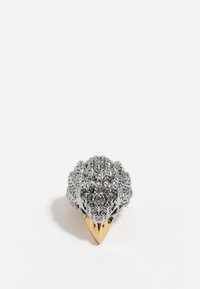 Anillo con diseño en relieve detallado y patrón de hojas plateadas, con una base dorada en forma cónica. La forma general recuerda a un elemento natural.