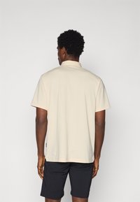 Polo de manga curta em bege claro, com colarinho clássico e textura suave, combinado com calções escuros.