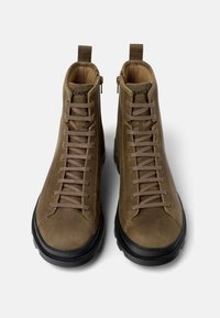 Botas de cuero marrón hasta el tobillo con cordones beige y suelas de goma negras. Detalle de cremallera en el lateral, costuras reforzadas a lo largo de los bordes.