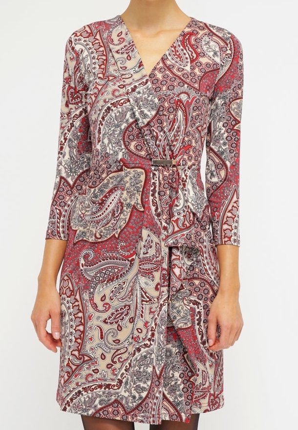 Femme portant une robe mi-longue avec des motifs cachemire rouges, blancs et noirs et des manches trois-quarts.