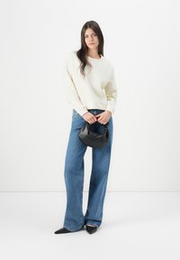 Cream sweatshirt, high-waisted blue wide-leg jeans, and a black faux leather handbag. The outfit features pointed black shoes.