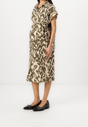 Pregnant woman wearing a short-sleeve belted midi dress with beige and olive animal print and black low-heeled loafers.