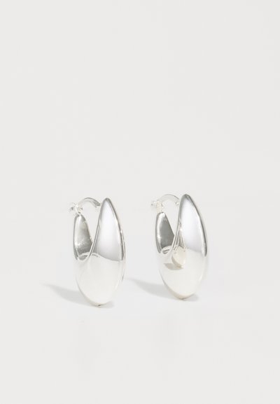Boucles d'oreilles en argent en forme d'anneau avec une surface lisse et réfléchissante, présentant une forme abstraite et allongée. Elles disposent d'une fermeture articulée pour un port sécurisé.