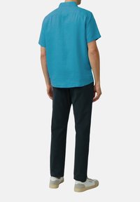 Korte mouwen overhemd van helderblauwe linnen, recht gesneden, met een standaard kraag, gecombineerd met donkere broek en beige sneakers.