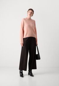 Pull en maille pêche avec un col rond et des manches larges. Associé à un pantalon large taille haute noir et des bottes à talons noires. Sac à main noir.