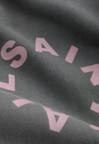 Detailný záber na sivú pletenú látku s ružovými písmenami vytvárajúcimi časť slova v zakrivenej línii.