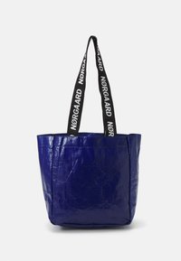 Sac fourre-tout bleu en matériau brillant avec une forme carrée. Dispose de poignées noires avec le texte blanc "NØRGAARD". Surface texturée, design simple.
