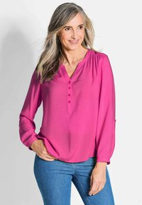 Fuchsia-farbene Bluse mit langen Ärmeln, V-Ausschnitt und einer Knopfleiste mit fünf Knöpfen, die eine lockere Passform und Raffungen an den Schultern aufweist.