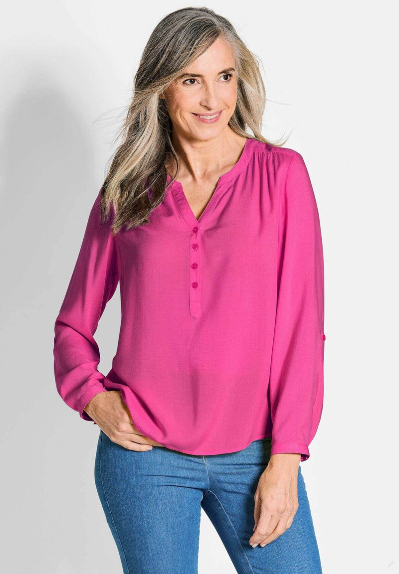 Fuchsia-farbene Bluse mit langen Ärmeln, V-Ausschnitt und einer Knopfleiste mit fünf Knöpfen, die eine lockere Passform und Raffungen an den Schultern aufweist.
