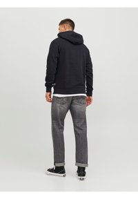 Felpa nera con un ampio cappuccio, polsini a costine e orlo. Abbinata a jeans grigi e sneakers nere alte. Design semplice, senza motivi visibili.