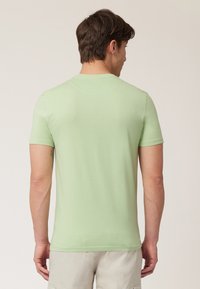 T-shirt kratkih rukava, prilagođenog kroja, izrađen od svijetlozelene cotton, s okruglim izrezom i glatkom teksturom, prikazan sa stražnje strane.