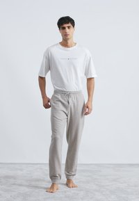 Îmbrăcăminte pentru bărbați formată dintr-un tricou din bumbac alb cu logo imprimat și pantaloni scurți gri cu șnur și manșete elastice.