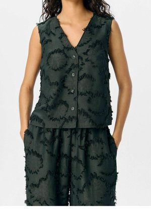 Sleeveless black button-up top and matching pants with textured circular patterns worn by a standing person with hands in pockets.