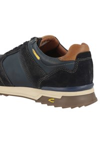 Sportschoen in een mix van marineblauw leer en zwart suede, met een tan hielaccent en een beige rubberen zool met gele details.