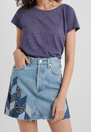 Fioletowa koszulka z krótkim rękawem w połączeniu z jasnoniebieską spódnicą dżinsową z patchworkowym wzorem w różnych odcieniach niebieskiego i białymi wzorami.
