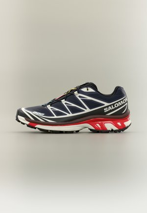 Salomon running shoe in navy blue with white and red accents. Features a textured upper, contoured sole, and secure lace system for support.