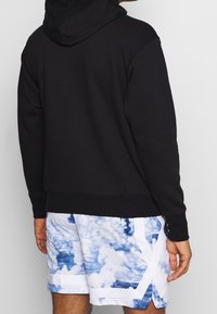 Czarna bluza z kapturem o miękkiej fakturze. W połączeniu z szortami w niebiesko-białe chmurki z białymi akcentami.