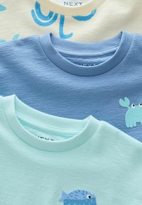 Två texturerade T-shirts syns: en blå tröja med ett krabban grafik och en ljus mintfärgad tröja med ett fisk grafik, alla med kontrasterande halsringningar.