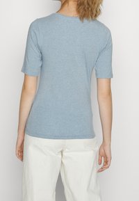 Ljusblå t-shirt med kort ärm och rund halsringning i mjukt material, kombinerad med ljusa vida byxor.